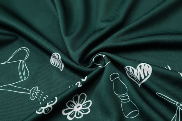 A close-up of dark green fabric featuring a pattern of white floral and gardening illustrations.
