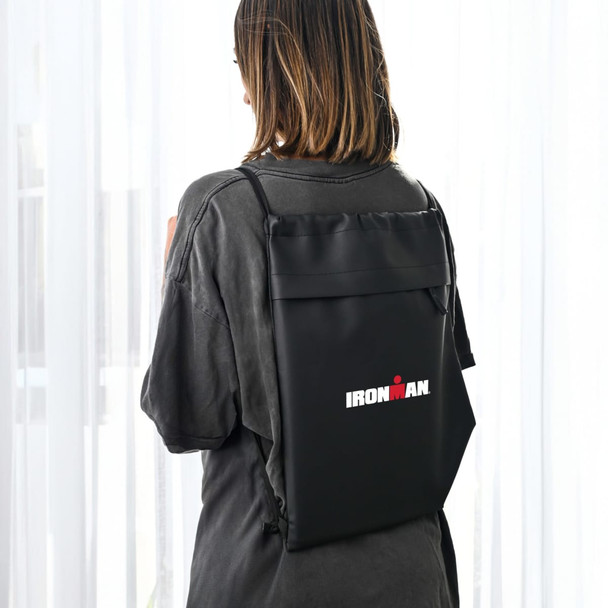 A black drawstring bag with a logo, worn on the back of a person, featuring a sleek design.