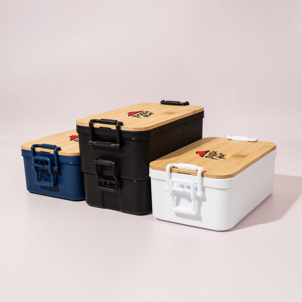 Three lunch boxes in navy, black, and white with bamboo lids and handles. All feature a logo on the top.