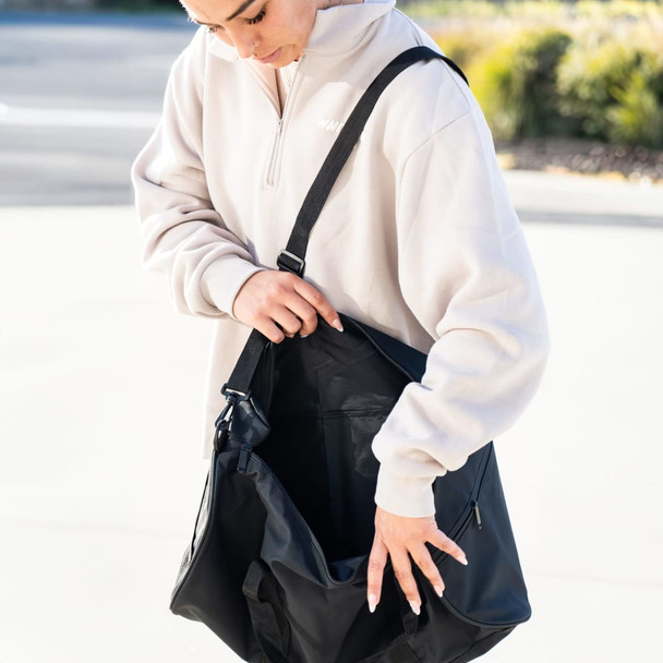 A black duffle bag with an adjustable strap, being held open by a person in a light-coloured top.