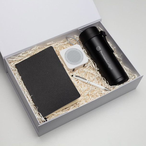 A black drink bottle, notebook, white speaker, and pen in a gift box with shredded paper filling.