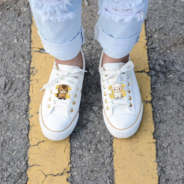 White sneakers adorned with novelty glowing clog shoe charms featuring a bear and a cow, set on a paved surface.