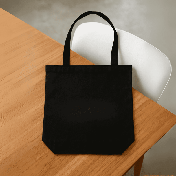 A black tote bag with two handles, placed on a wooden table. The bag has a logo on the front.