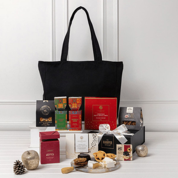 A black tote bag filled with assorted gourmet treats, including chocolates, biscuits, and festive snacks in decorative packaging.