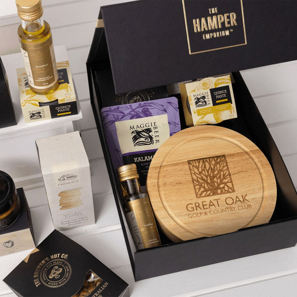 A gourmet gift set featuring a wooden board, various condiments, snacks, and a branded box. Includes purple and gold packaging.
