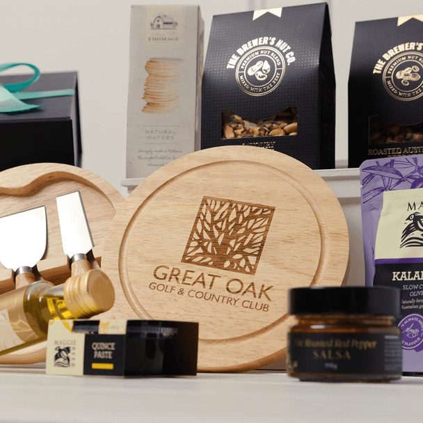 A wooden serving board with utensils, gourmet condiments, snacks in black packaging, and a jar of roasted red pepper salsa.