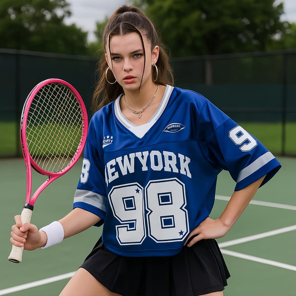 A young woman poses in a blue jersey featuring white text and a number, holding a pink tennis racket on a court.