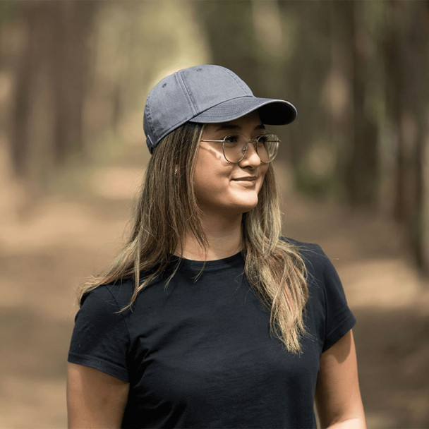 A grey organic washed cotton cap worn by a person in a wooded setting, featuring a logo on the front.