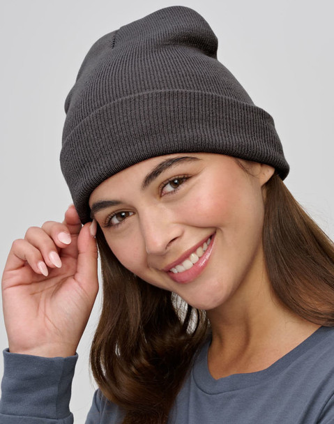 A dark grey beanie made from recycled materials, worn by a smiling woman, featuring a simple ribbed design.