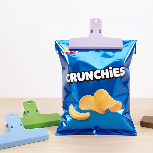 A bag of blue snack chips with a purple plastic clip, accompanied by green and brown plastic clips on a wooden surface.