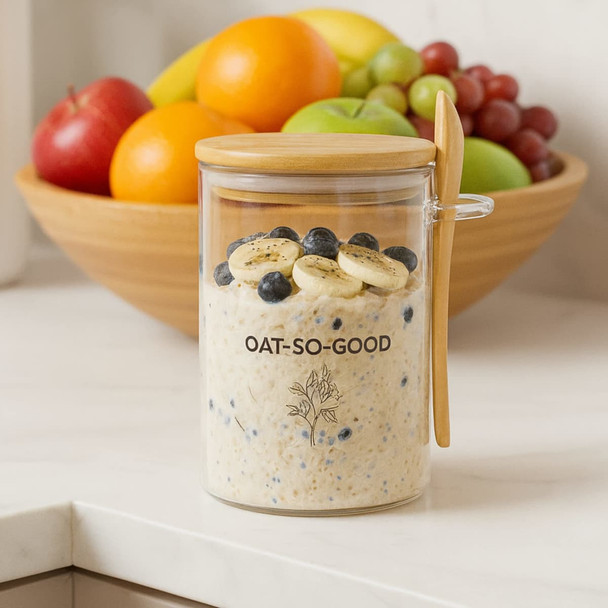 A glass container with oats, topped with banana slices and blueberries, featuring a wooden lid and branding.