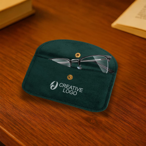 A green velvet glasses pouch with a logo, partially opened to display a pair of glasses inside, placed on a wooden surface.