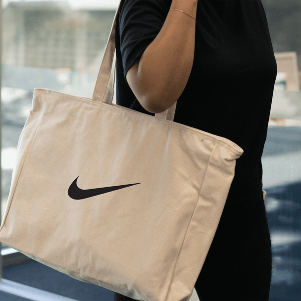 A large cream tote bag with a black logo being held by a person.