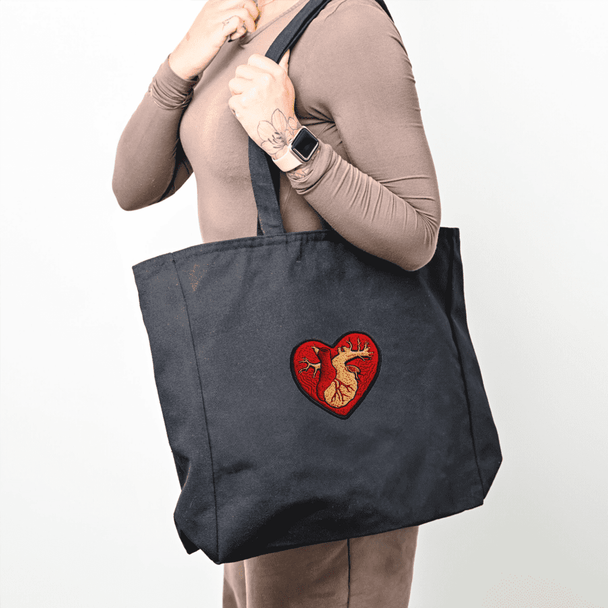 A large black tote bag with a heart-shaped design featuring a dragon, held by a person.