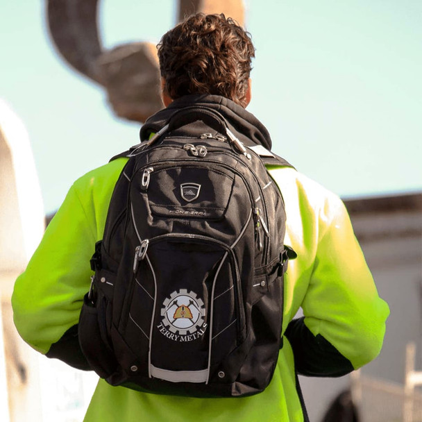 A black High Sierra Elite Fly-By 17" computer backpack with a logo, worn by a person in a high-visibility jacket.