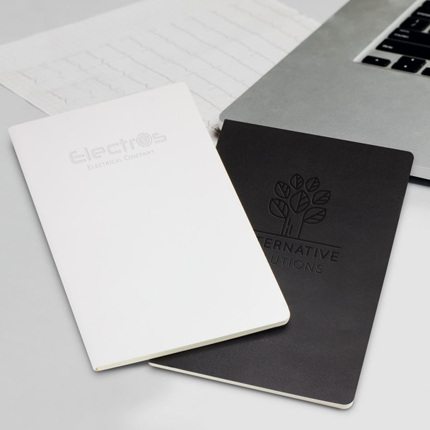 Two Moleskine Volant journals, one white and one black, placed beside a laptop and a notepad. Each has a logo on the cover.