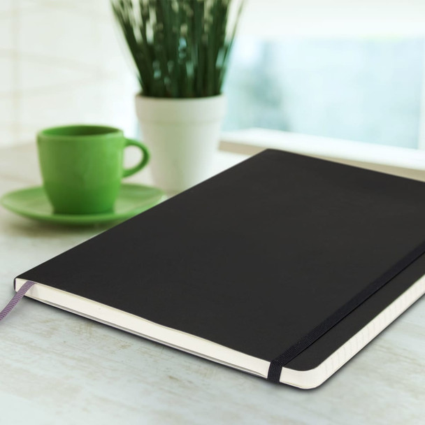 A black soft cover notebook sits on a desk, accompanied by a green cup and a potted plant in the background.