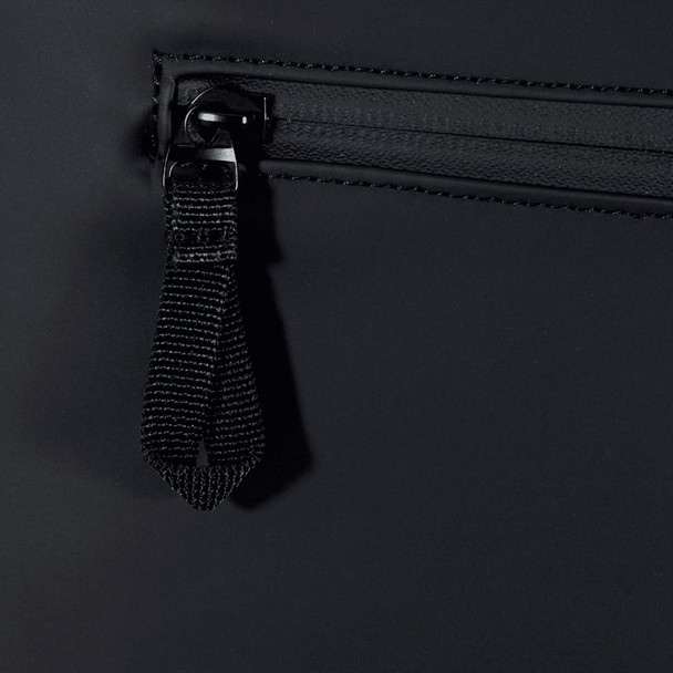 A close-up of a black backpack zipper with a fabric pull tab. The material appears water-resistant.