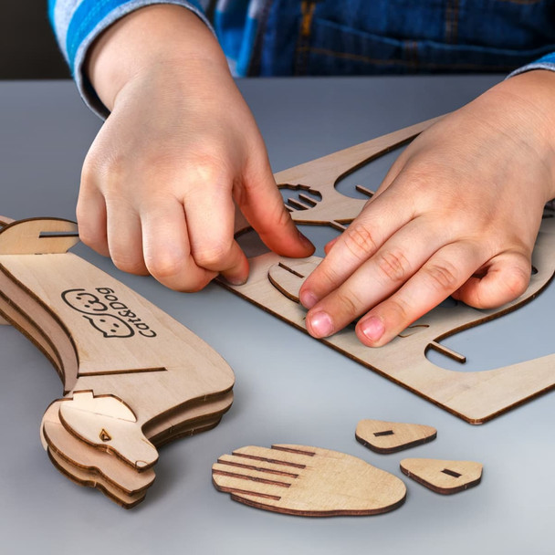 A wooden model of a dog being assembled with hands arranging various pieces on a flat surface.