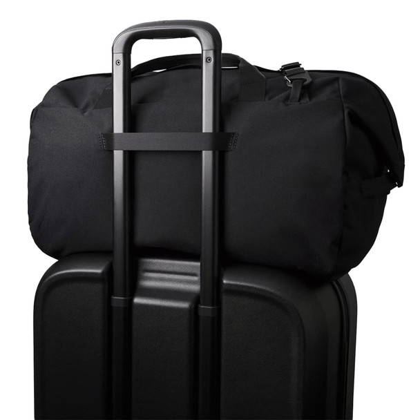 A black duffel bag sits on top of a black suitcase, featuring a trolley handle for easy transport.