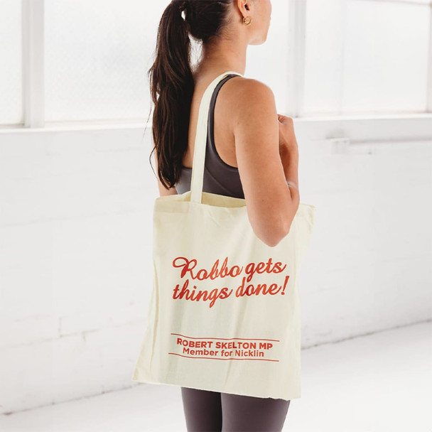 A calico tote bag in cream colour featuring a logo and text. A person holds it while wearing activewear.