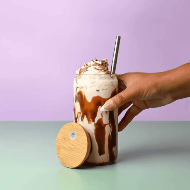 A drink bottle with a bamboo lid, featuring a creamy beverage topped with whipped cream, held in a hand.
