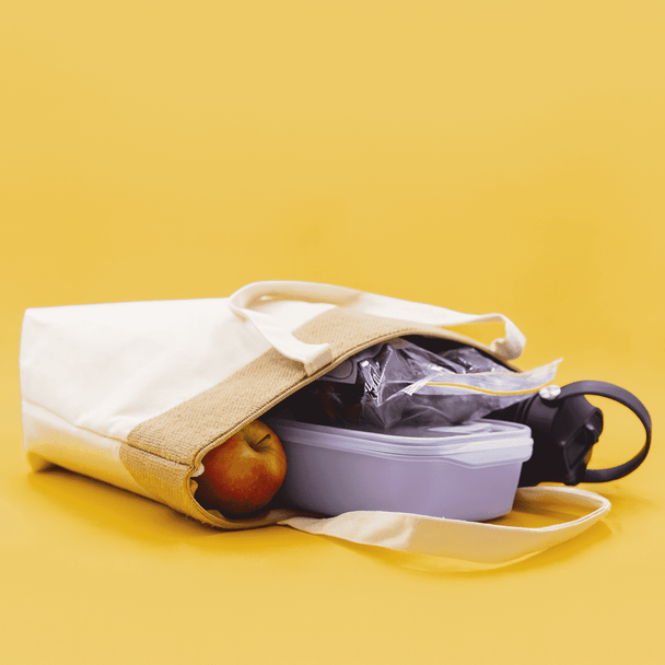 A jute and cotton cooler bag with a drink bottle, a food container, and an apple inside, featuring a neutral colour scheme.