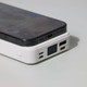 A white power bank with a digital display, featuring multiple ports, placed beside a smartphone.