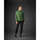 A woman stands wearing a green Women’s Kyoto Jacket paired with black leggings and shoes, with a dark background.