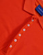 An orange polo shirt with a collar and a button placket. It features a branding label on the inside.