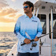 A men's long-sleeve fishing polo in light blue ombre design, featuring a logo, with a person holding a fishing rod.