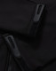 Close-up of a black softshell jacket featuring zippers and velcro details. The jacket has a logo on it.
