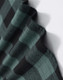 A close-up of a unisex flannel shirt in black and green plaid fabric, featuring a logo.