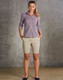 A model wearing khaki chino shorts paired with a button-up shirt, standing against a textured grey background.