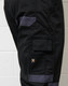 A close-up of black cargo pants featuring grey accents and a logo on the side.