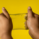 A pair of hands stretching a translucent yellow jelly cube sensory toy against a bright yellow background.
