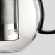 A glass tea press featuring a stainless steel infuser and a black handle, with a logo on the body.