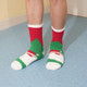 A pair of cosy socks featuring a red, green, and white design, worn on feet standing on a blue floor.