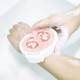 A pink and white expandable dishwashing sponge held in soapy hands over a sink.