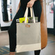 A beige and cream tote bag with a logo, held by a person, containing various items inside.