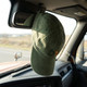 A green vintage washed cap hanging from the mirror inside a vehicle, with a logo on the front.