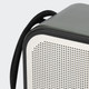 A grey and white portable speaker with a textured surface and a black strap attached.