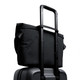 A black messenger bag positioned on top of a wheeled suitcase, featuring a retractable handle.