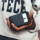 A hand holding a black and grey Thread Zipper Wallet, featuring a zippered compartment and a card slot.