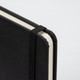 A4 daily diary in black with an elastic band closure and rounded corners. Features a textured cover and plain pages.