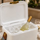 A white cooler filled with ice and a bottle of wine, featuring a gold latch and a striped handle.