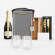 A grey insulated hamper containing a bottle of sparkling wine, two glass tumblers, a wooden cutting board, and a knife set.