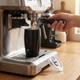 A drink bottle with a sleek black design and a branding logo, positioned under an espresso machine.