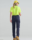 A woman wearing a bright yellow shirt and navy flexi work pants, seen from the back, with a cap and boots.