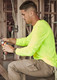 A man works in a construction setting, wearing a neon yellow long sleeve tee and beige cargo pants, using pliers.